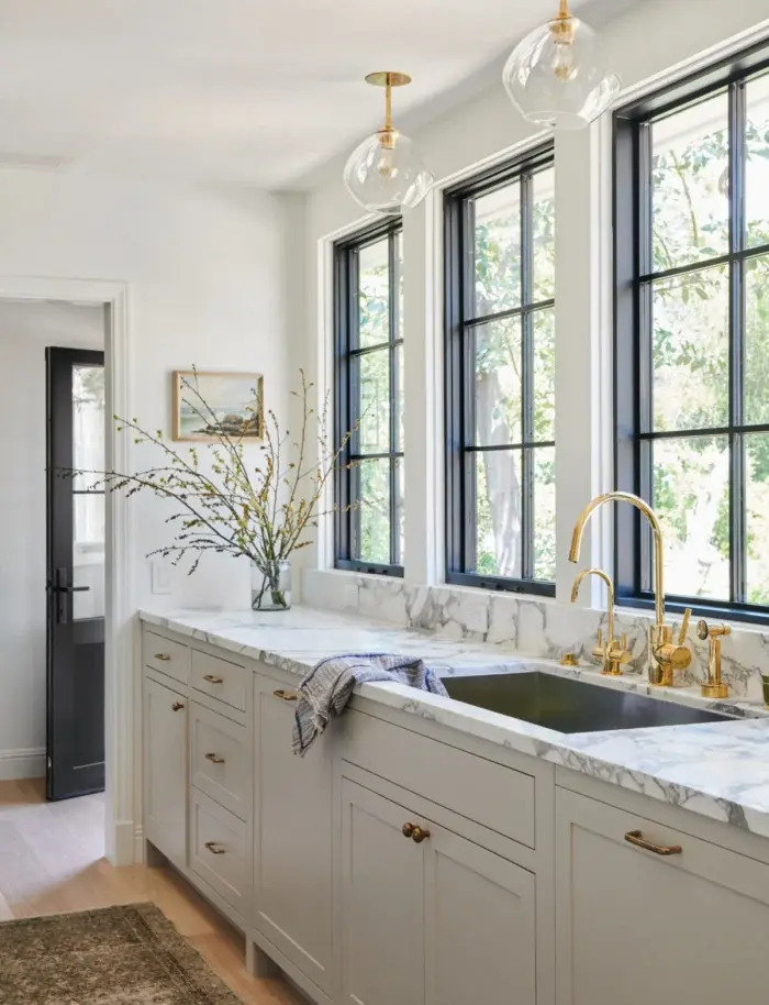 This beautiful gray and white kitchen, with its brass accents and black framed windows, is a beautiful blend of modern and traditional design, from Amber Interior Design - Photo Tessa Neustadt